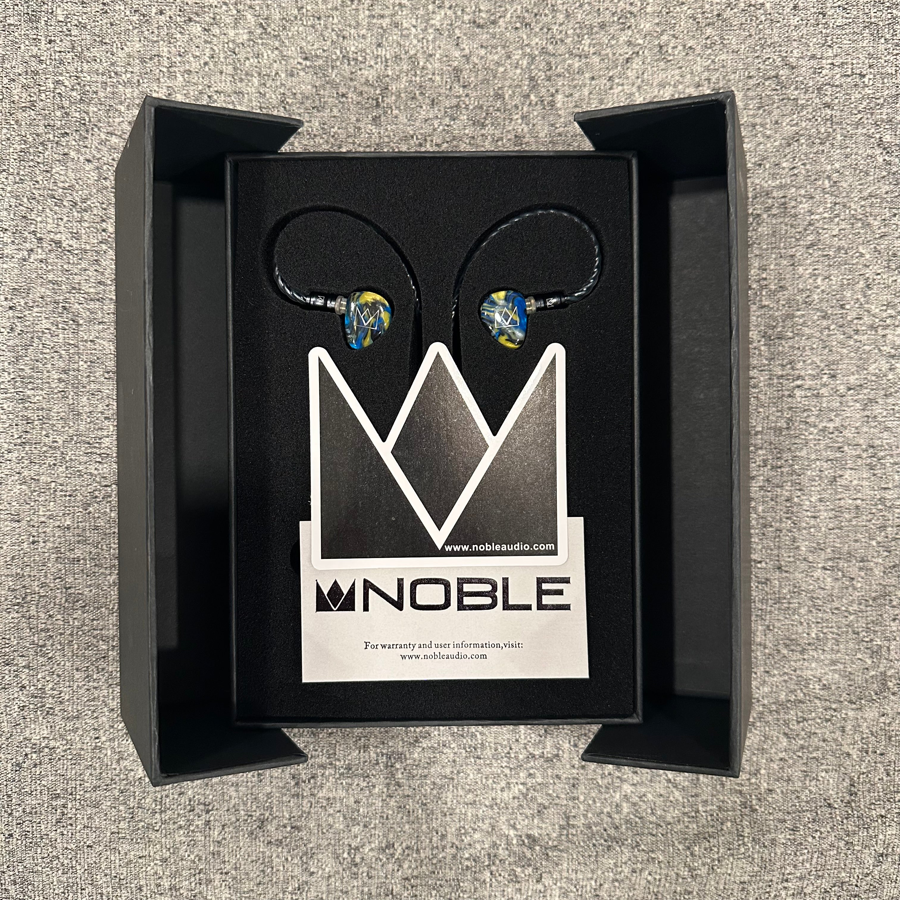 Noble audio earbuds in a black box on a textured gray background